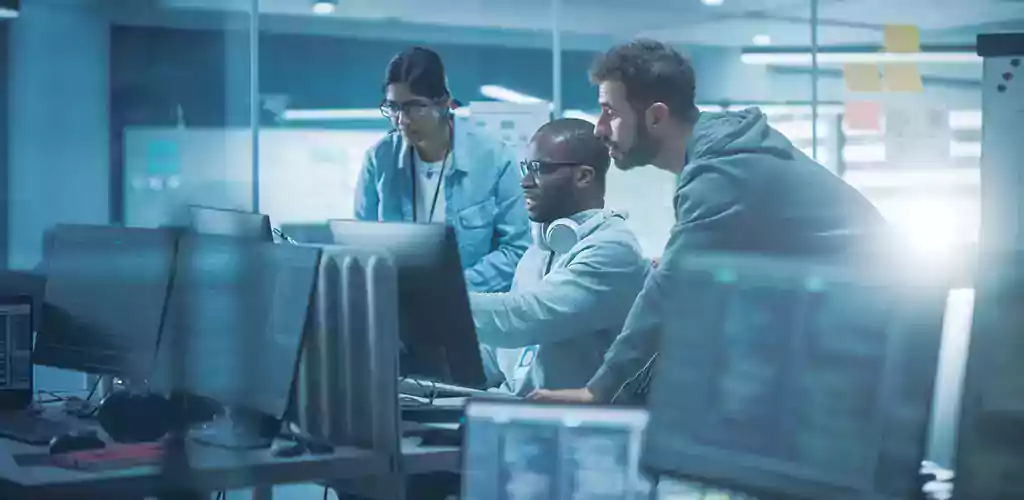 3 people sitting at a long desk working on laptops.