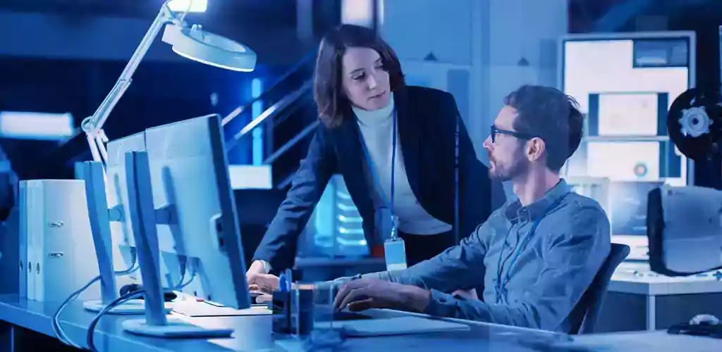 Two agents chat in front of a computer in an office.