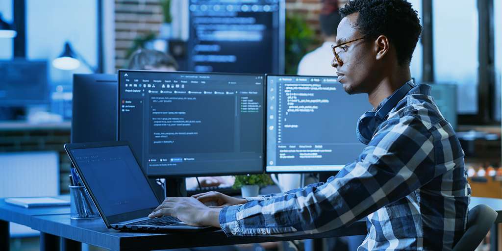 Man working on a laptop with 2 additional monitors